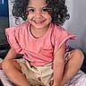 Amalia joined the competition — help win amazing prizes! child, smiling, curly_hair, pink_shirt, shorts, indoor, quilted_surface, cross_legged, happy, cute, portrait, person, young, sitting, feet, face, playful, casual_clothing, home, light