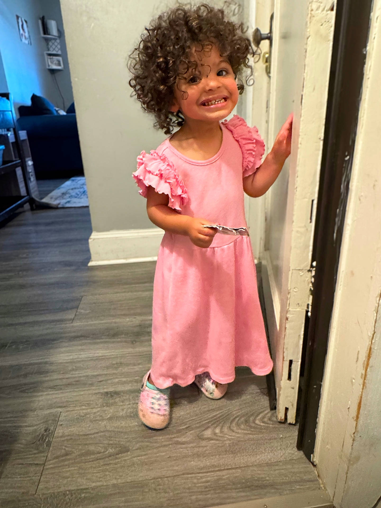 Amalia joined the competition — help win amazing prizes! child, curly_hair, cute, door, floor, hand, happy, home, indoor, light, person, pink_dress, portrait, slippers, smiling, standing, toddler, wall, wooden_floor, young