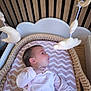 baby, bassinet, bedroom, chevron_pattern, child, cozy, crib, cute, gazing, hanging_toys, indoors, infant, newborn, pink_clothing, plush_toys, resting, sleeping_area, soft_toys, wicker, wooden_crib