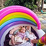 baby, blanket, blue, child, colorful, green, hand, infant, inflatable_pool, outdoor, pink, plant, purple, rainbow, relaxed, summer, sunglasses, toy, tree, yellow