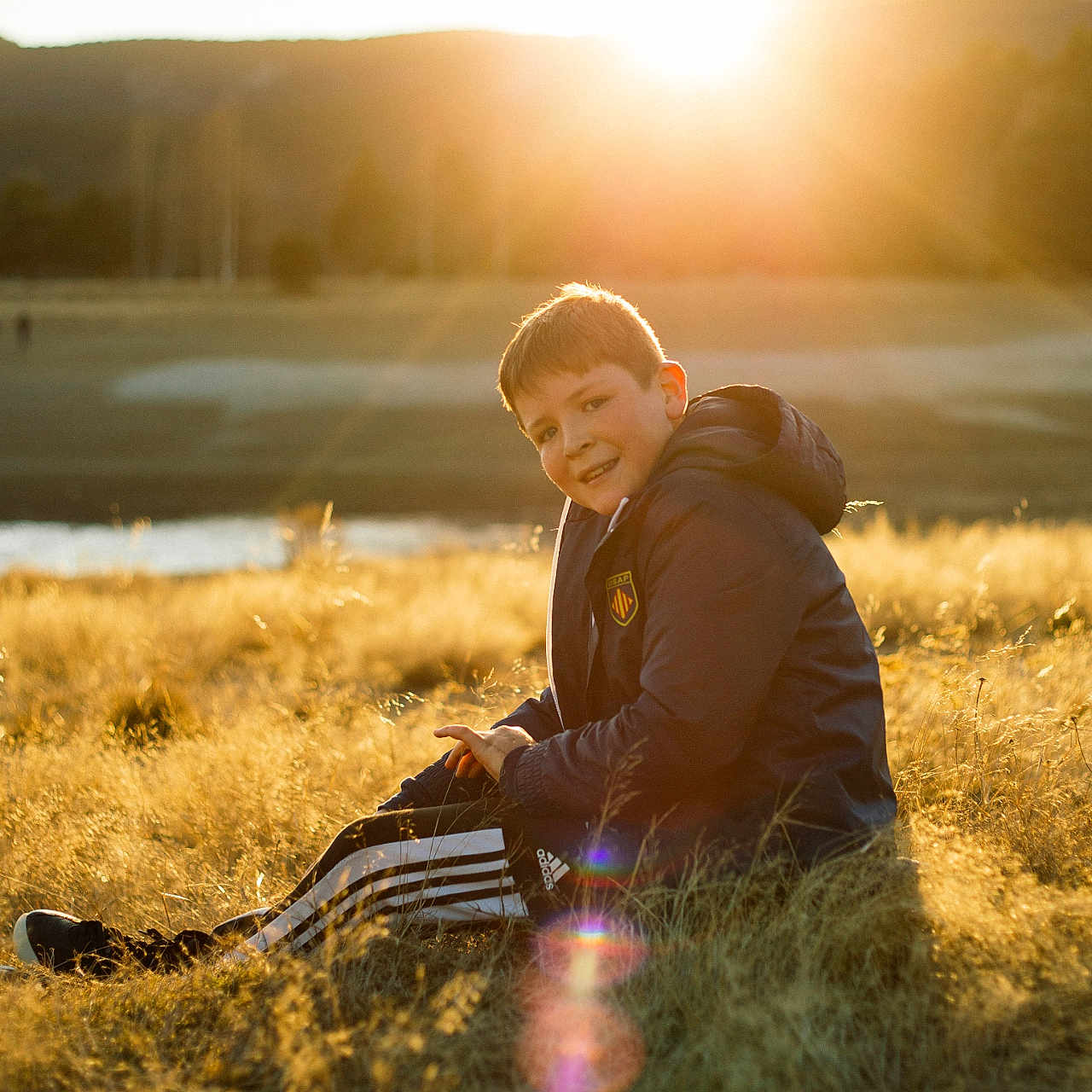 Mattéo a rejoint le concours — aidez-le/la à gagner de superbes lots ! boy, child, clothing, coat, face, flare, grass, head, jacket, light, male, nature, outdoors, person, photography, plant, portrait, sitting, sky, sunlight