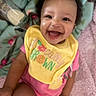 baby, smiling, happy, child, infant, bib, pink_clothing, yellow_bib, blanket, soft, indoors, cute, joyful, portrait, sitting, face, human, young_child, expressive, cheerful