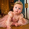 Iliana is registered to the contest to win money with this photo: baby, child, princess, tiara, pink_dress, sparkles, crawling, wooden_floor, blue_door, jewelry, indoor, portrait, cute, glowing, costume, face, eyes, hand, floor, lighting