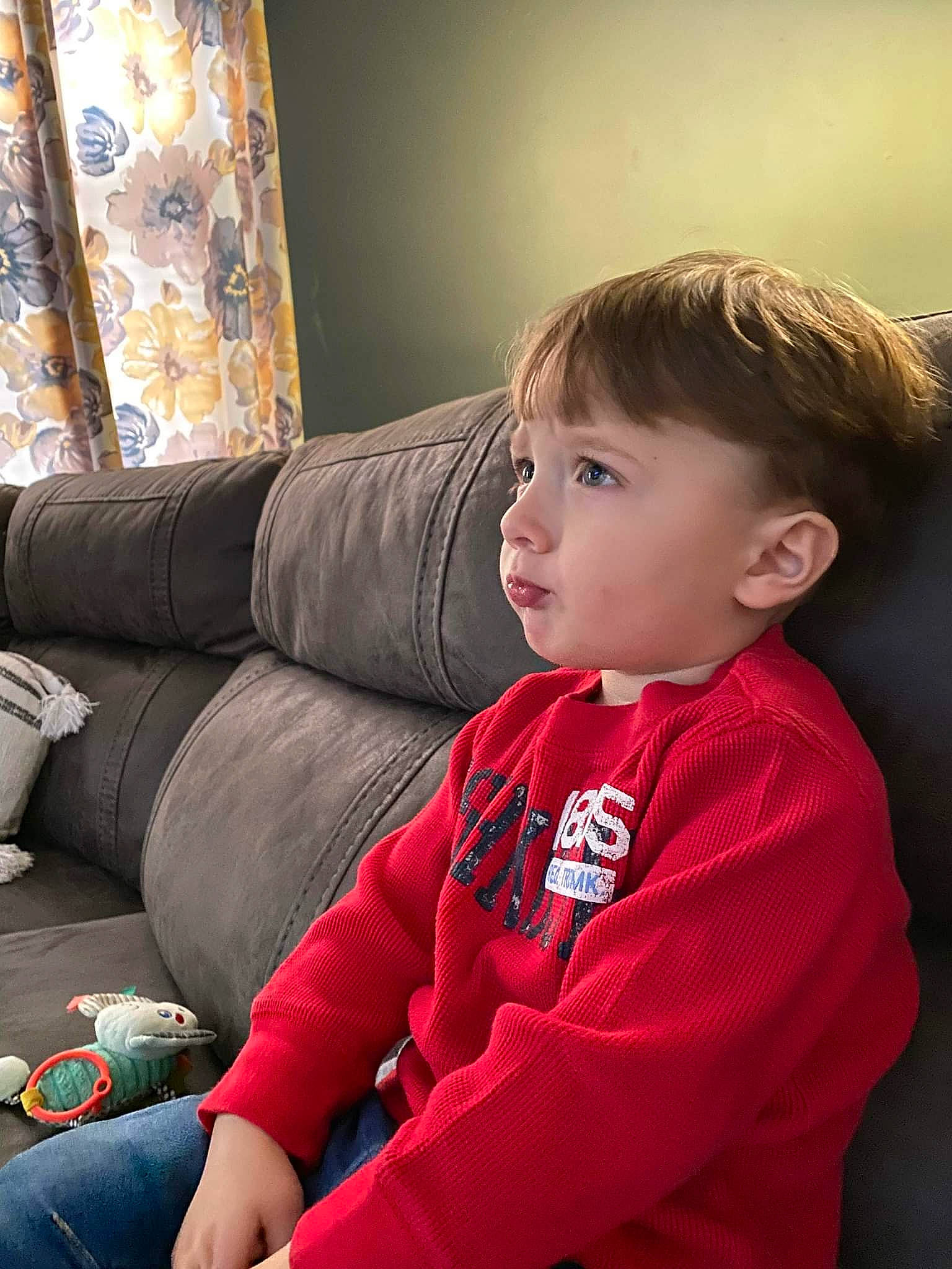 Justin is registered to the contest to win money with this photo: baby_toddler_clothing, carmine, cheek, child, comfort, couch, curtain, elbow, flooring, hair, human_leg, knee, lap, living_room, person, room, sitting, sleeve, thigh, toddler