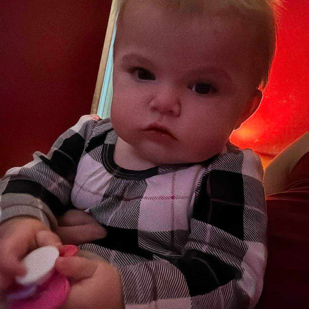 Lidia is registered to the contest to win money with this photo: baby, blonde_hair, child, closeup, cozy, cute, expression, face, hand, holding, indoor, infant, pacifier, person, plaid_clothing, portrait, red_wall, sitting, soft_lighting, young_child