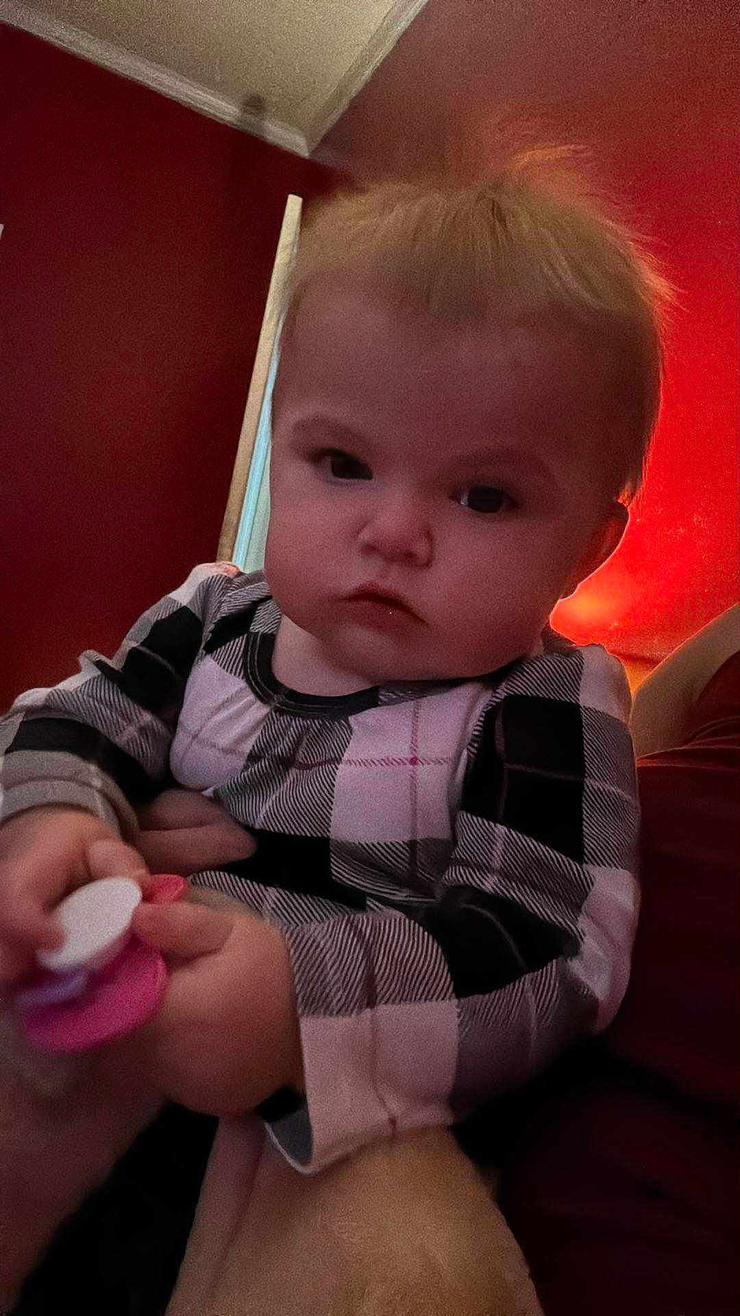 Lidia is registered to the contest to win money with this photo: baby, child, infant, plaid_clothing, pacifier, indoor, person, face, hand, red_wall, blonde_hair, expression, closeup, portrait, young_child, cute, holding, sitting, soft_lighting, cozy