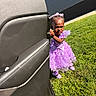 child, toddler, purple_dress, grass, car_door, outdoor, sunlight, portrait, cute, determined, young_girl, fashion, feet, hair_bows, expression, people, daylight, wall, sidewalk, shoes