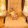 baby, infant, chair, beige, onesie, carpet, stone_wall, indoor, furniture, person, seat, small, cute, child, young, office_chair, floor, relaxed, happy, cozy