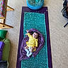 Bailey is registered to the contest to win money with this photo: baby, infant, yellow_clothing, purple_blanket, teal_cloth, yoga_mat, floor, cushions, chair, colorful, indoor, raising_hand, lying_down, comfort, blanket, head, face, socks, home, relaxation