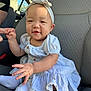 baby, child, car_seat, dress, headband, drool, hand_holding, infant, cute, smiling, person, sitting, white_socks, car_interior, young_child, portrait, skin, fingers, fabric, seat