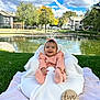 baby, infant, smiling, pink_clothing, knitted_outfit, headband, cushion, blanket, grass, outdoor, pond, trees, blue_sky, clouds, wooden_sign, five_months, happy, child, portrait, nature