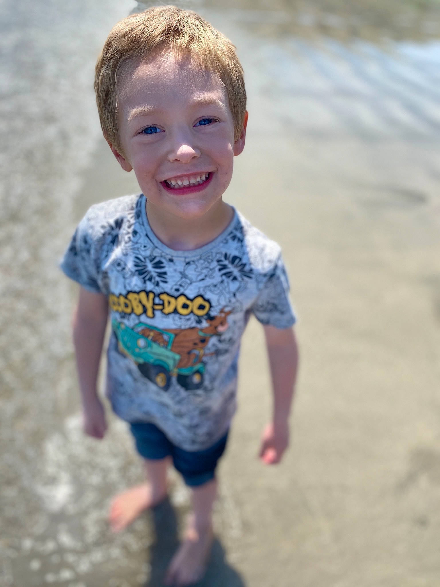 Finlee is registered to the contest to win money with this photo: beach, blue, child, facial_expression, fun, happy, joy, person, play, sand, sea, skin, smile, standing, summer, t_shirt, toddler, vacation, water