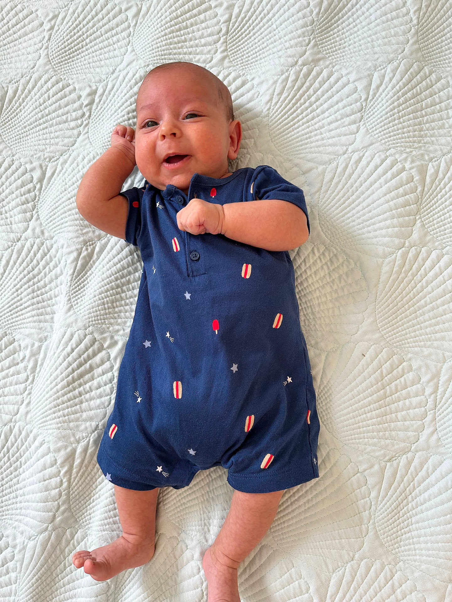 Kaya joined the competition — help win amazing prizes! baby, infant, smiling, blue_clothing, romper, lying_down, quilt, white_background, cute, happy, child, newborn, skin, face, hand, foot, patterned_clothing, indoors, soft_texture, relaxed