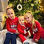 child, baby, christmas_tree, holiday, festive_clothing, red_outfit, carpet, living_room, smiling, family, indoors, decorations, fairy_lights, sitting, toy, happy, blonde_hair, cute, seasonal, portrait