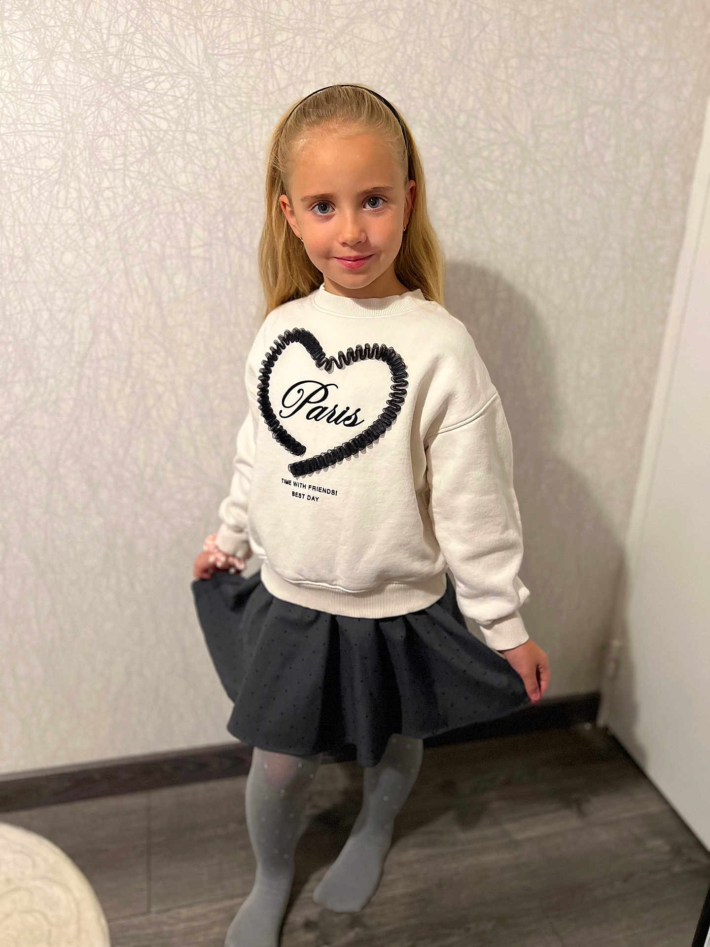 Daria participe au concours pour gagner de l'argent avec cette photo : child, girl, blonde_hair, headband, white_sweatshirt, black_heart, paris_text, black_skirt, gray_tights, indoor, wooden_floor, patterned_wall, smiling, posing, standing, fashion, casual_clothing, young, cute, portrait