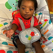 Terrell joined the competition — help win amazing prizes! animal_design, baby, baby_seat, bright_colors, child, colorful, curly_hair, cute, indoor, infant, orange_shirt, patterned, plant_design, playful, reaching_hand, seat_cushion, smiling, straps, toddler, wooden_floor