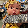 Kehlani joined the competition — help win amazing prizes! baby, child, infant, headband, yellow, bow, face, eyes, tongue, clothing, patterned, baby_carrier, person, indoor, restaurant, people, blurred_background, cute, closeup, expression