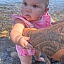 baby, child, water, tattoo, arm, pink_clothing, outdoor, rocks, shore, holding, curious, barefoot, summer, nature, person, skin, face, hand, legs, sunlight