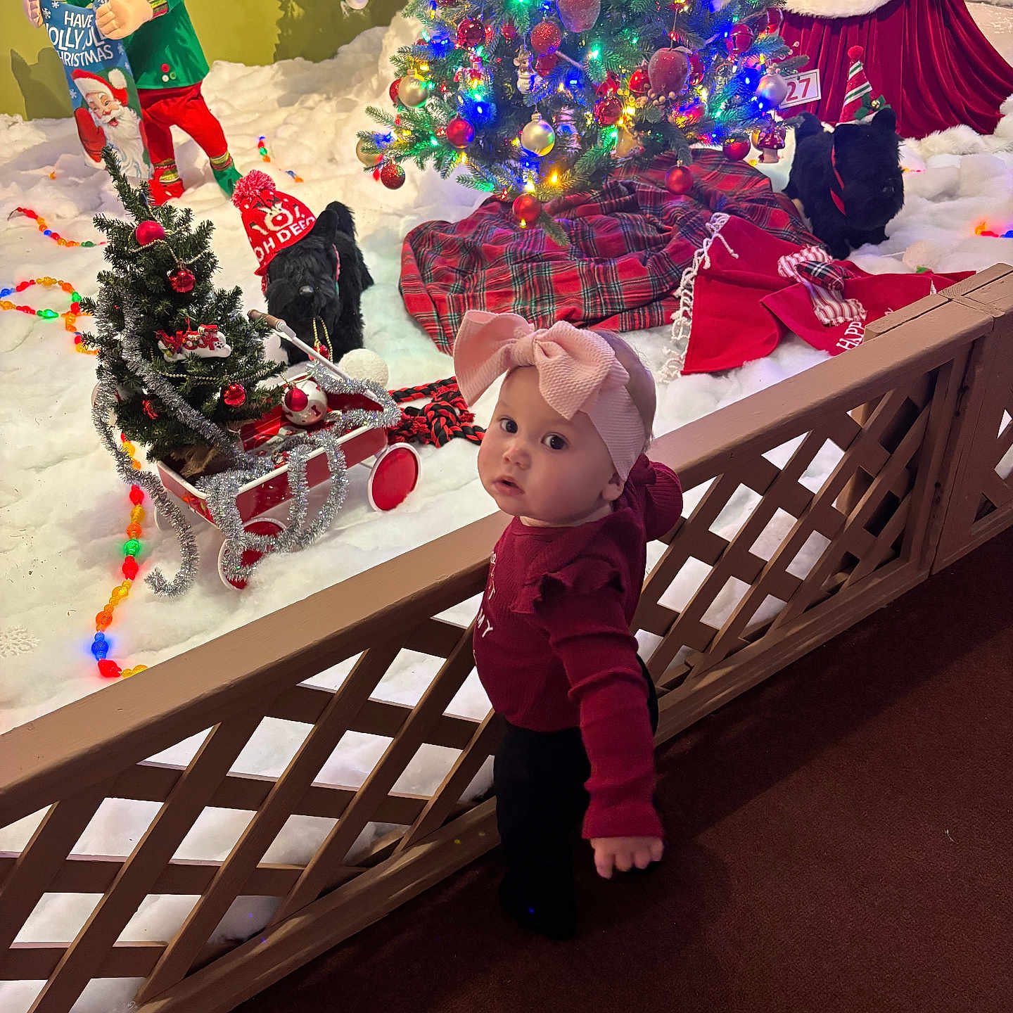 Kehlani joined the competition — help win amazing prizes! black_dog, carpet, child, christmas_tree, curious_expression, decorations, dog_hat, elf_figure, festive, festive_clothing, holiday_lights, holiday_scene, indoor, mini_sleigh, pink_bow, plush_toys, red_sweater, snow_decor, toddler, wooden_fence