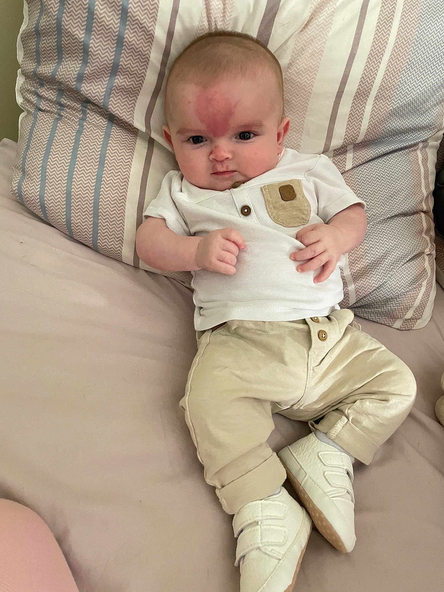 Eloann a rejoint le concours — aidez-le/la à gagner de superbes lots ! baby, infant, bed, pillow, clothing, white_shirt, beige_pants, white_shoes, face, person, cute, indoors, young_child, patterned_pillow, resting, lying_down, casual, comfortable, expression, small
