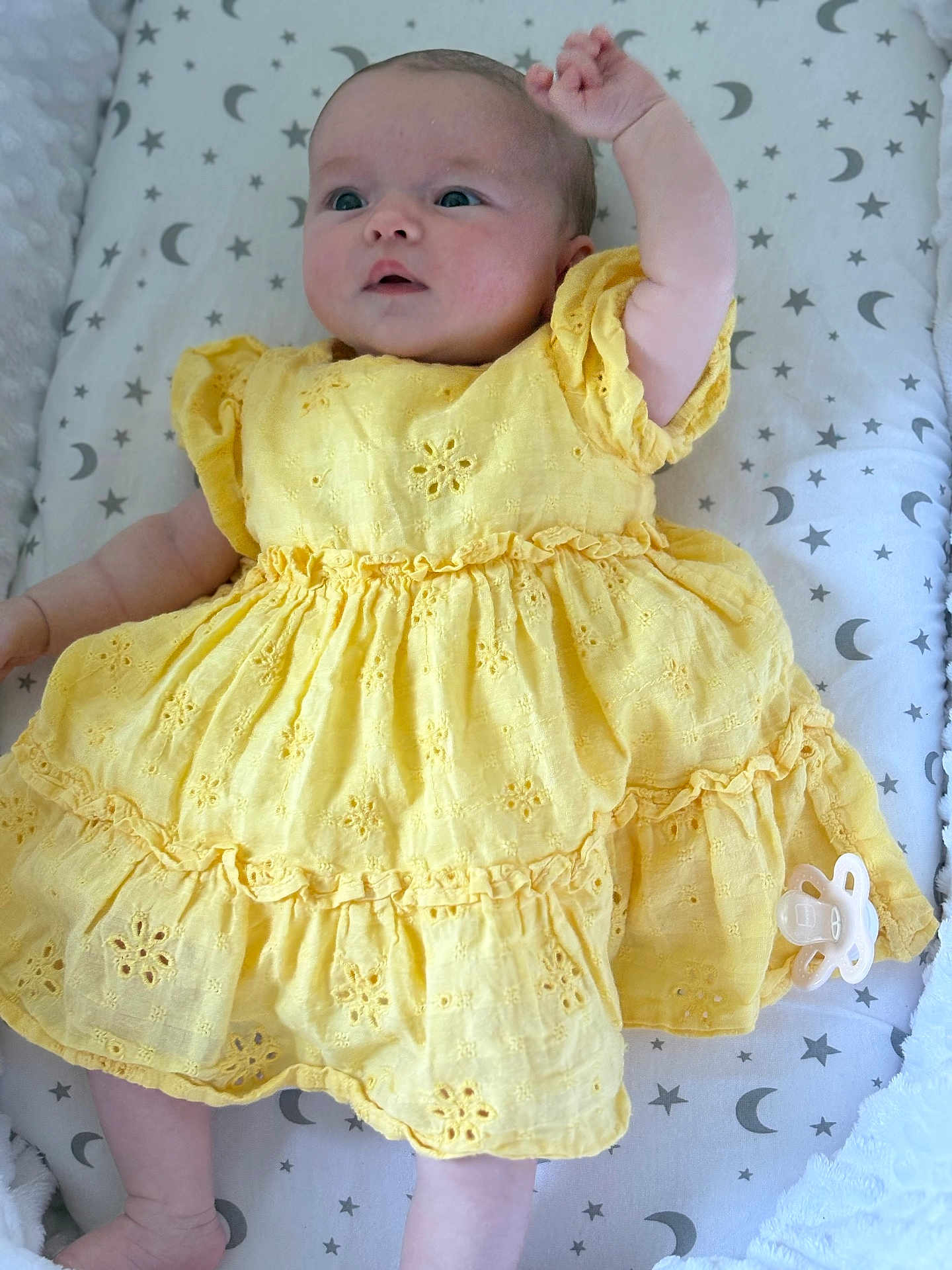 Konnie is registered to the contest to win money with this photo: baby, yellow_dress, infant, lying_down, raised_arm, pacifier, patterned_bedding, stars, moons, soft_texture, cute, child, portrait, sleeping_area, adorable, clothing, fabric, newborn, resting, indoor
