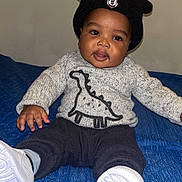 Lyam-Rafaël participe au concours pour gagner de l'argent avec cette photo : baby, child, sweater, hat, black_hat, dinosaur_print, blue_blanket, white_shoes, smiling, sitting, indoor, cute, portrait, clothing, footwear, happy, person, infant, cozy, playful