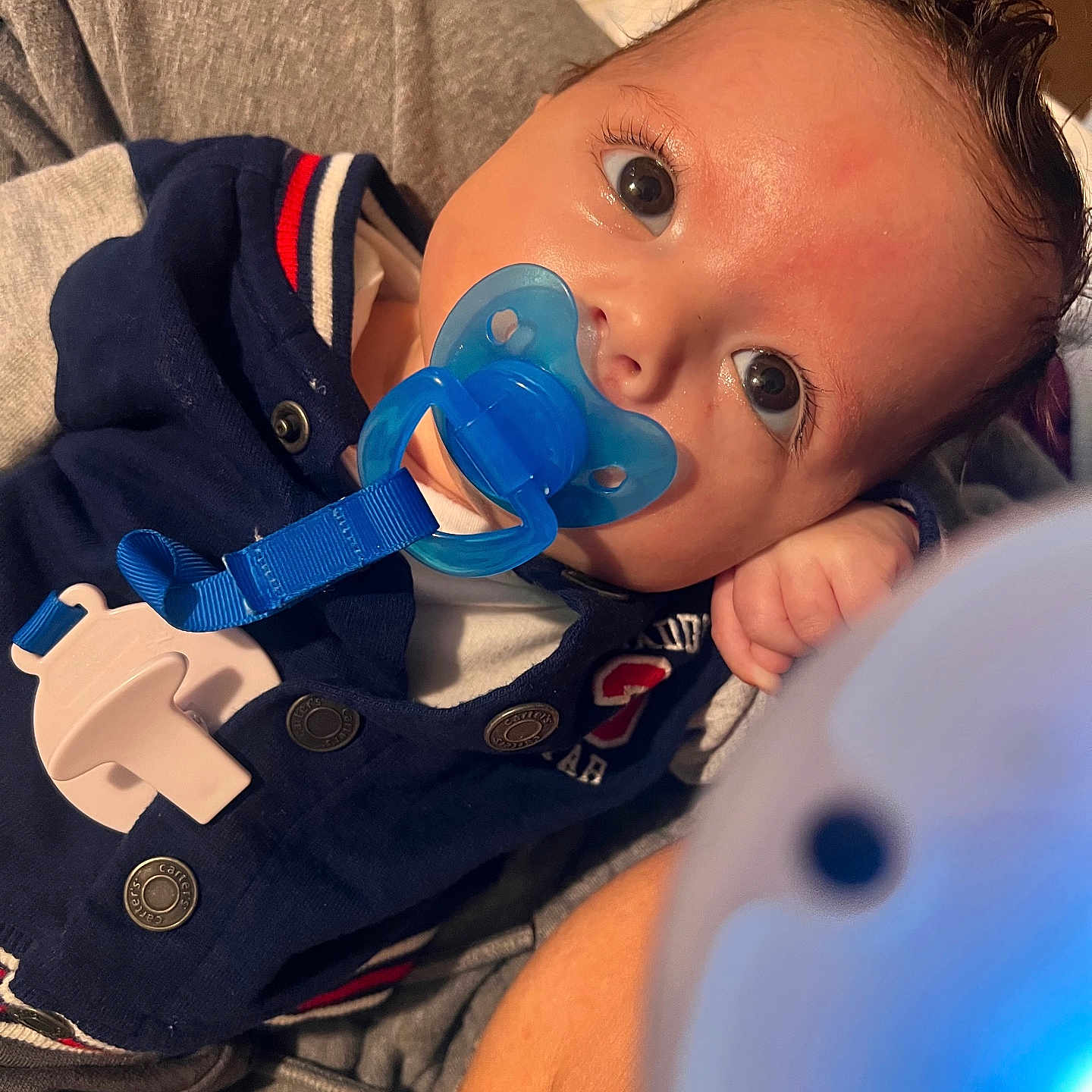 Amariyon is registered to the contest to win money with this photo: baby, blue, button, child, closeup, clothing, comfort, cute, eyes, fabric, face, hair, hand, indoor, infant, pacifier, person, portrait, resting, skin