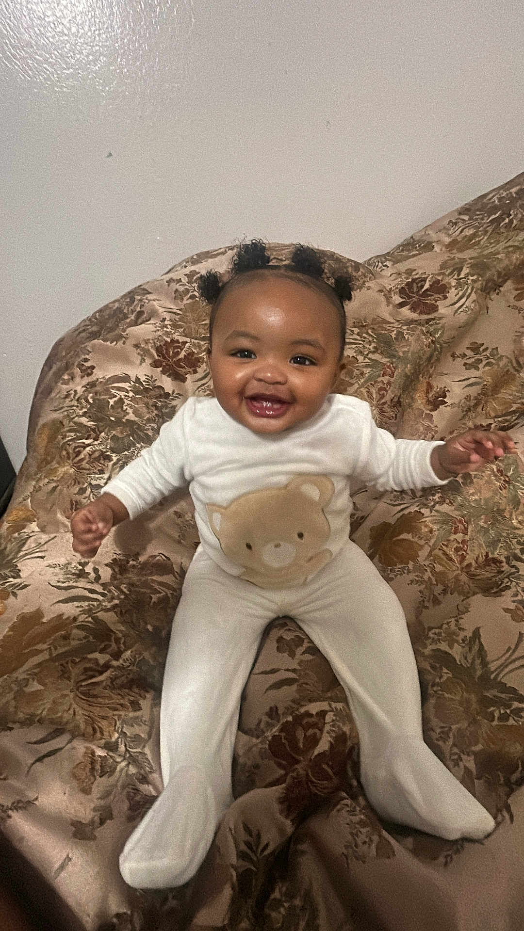 Khyla joined the competition — help win amazing prizes! baby, smiling, child, infant, white_outfit, teddy_bear, hair_puffs, couch, floral_pattern, indoors, happy, sitting, cute, portrait, young_child, cozy, furniture, person, face, expression