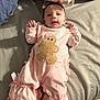 baby, infant, pink_outfit, headband, bow, bed, blanket, cute, sleepwear, gingerbread_man, child, person, indoor, soft_lighting, smiling, lying_down, furniture, cozy, adorable, portrait