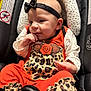 baby, infant, car_seat, headband, leopard_print, orange_clothing, child, cute, sitting, hand, face, apparel, patterned_clothing, indoor, closeup, portrait, infant_clothing, head_support, small_child, adorable