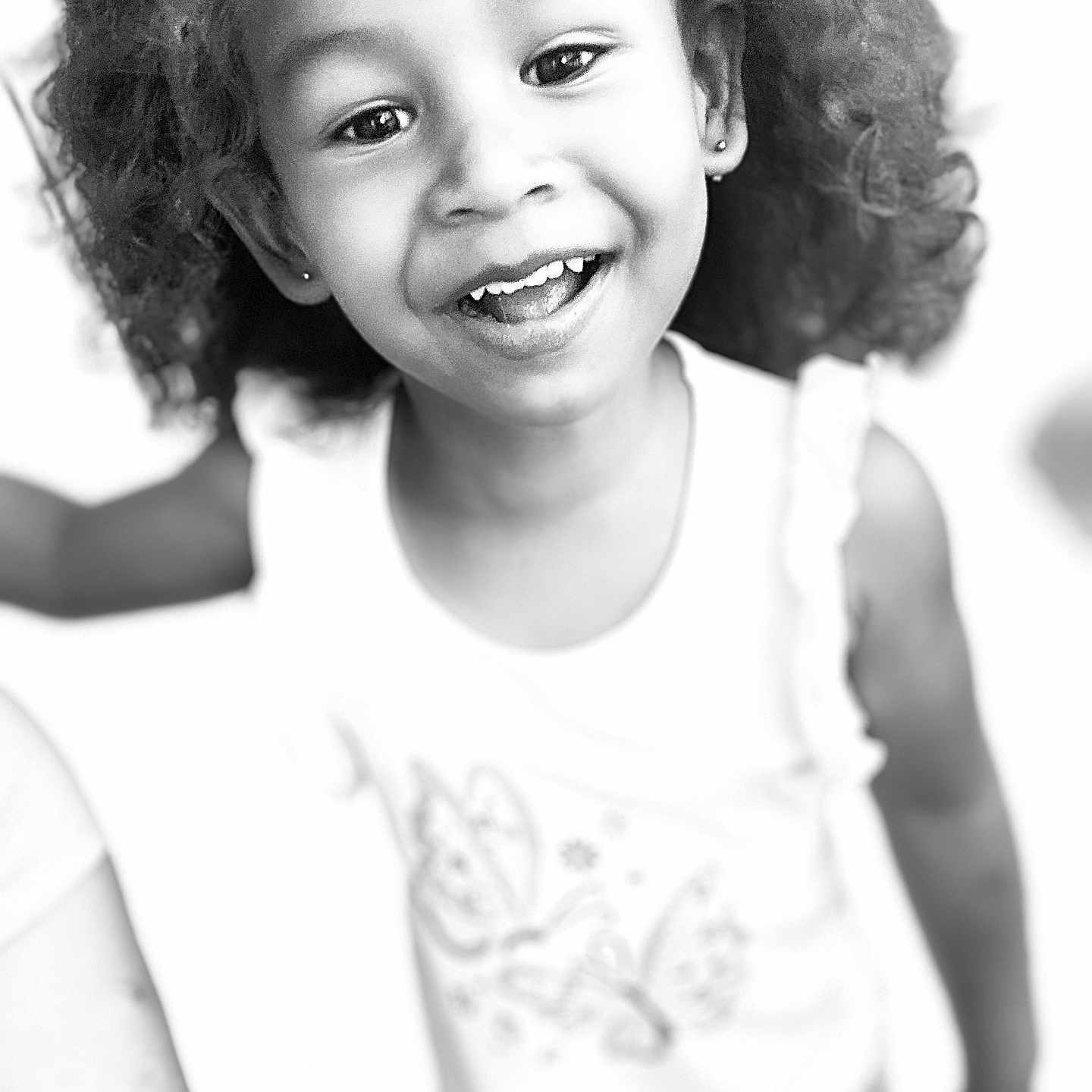 Avery is registered to the contest to win money with this photo: black_and_white, casual_clothing, child, close_up, curly_hair, cute, earrings, expression, face, happy, headband, indoor, joyful, person, playful, portrait, smiling, tank_top, toddler, young