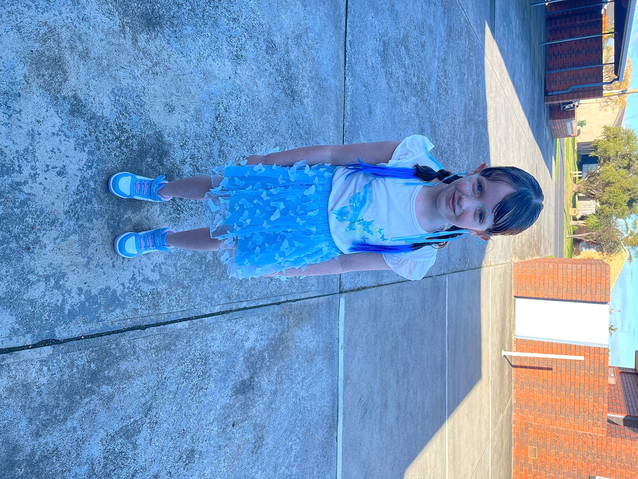Pippa is registered to the contest to win money with this photo: asphalt, azure, blue, building, cleanliness, composite_material, concrete, electric_blue, facade, flooring, joy, person, plant, road_surface, shadow, sidewalk, toddler, tree, walking_shoe