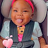 baby, child, car_seat, headband, pink_bow, tongue_out, smiling, toddler, cute, seatbelt, clothing, infant, portrait, indoor, playful, happy, person, baby_girl, sitting, heart_overlay