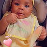 baby, infant, child, headband, bib, yellow_clothing, seat, cushion, cute, skin, hand, cloth, portrait, looking, indoor, adorable, pink_heart, text_overlay, face, eyes