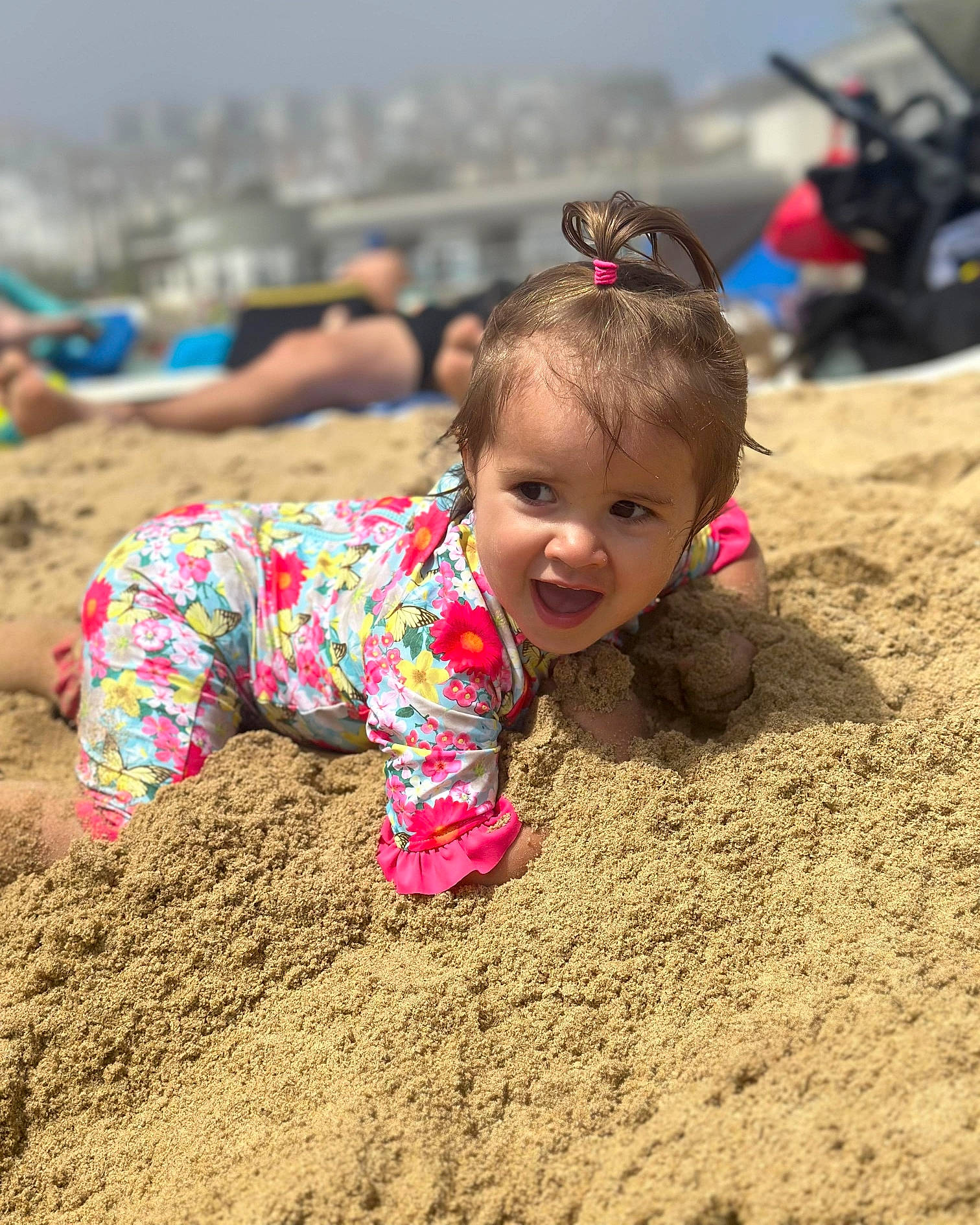 Clara is registered to the contest to win money with this photo: beach, body_of_water, child, fun, grass, happy, landscape, leisure, mud, people_in_nature, people_on_beach, person, play, recreation, sand, sitting, sky, smile, soil, toddler