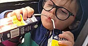 Greyson joined the competition — help win amazing prizes! child, glasses, hoodie, juice_box, car_seat, seatbelt, window, drinking, multitasking, casual_clothing, daylight, indoors, person, face, young_child, cute, playful, seat, relaxing, funny