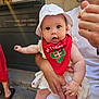 Julia participe au concours pour gagner de l'argent avec cette photo : adult_hand, arm, baby, bandana, casual_clothing, child, curious, daylight, dress, face, footwear, hat, holding, menu_board, outdoor, person, red_bandana, sidewalk, skin, white_hat