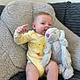 baby, child, plush_toy, stuffed_animal, yellow_onesie, baby_clothing, soft_furniture, couch, cozy, indoor, cute, infant, smiling, expression, comfort, seated, toddler, hand_gesture, face, hair