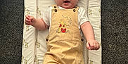 Louie joined the competition — help win amazing prizes! baby, child, infant, overalls, yellow_clothing, white_shirt, socks, changing_mat, bunny_pattern, carpet, floor, happy, smiling, cute, indoor, person, small_child, playful, clothing, light