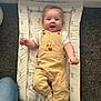 baby, child, infant, overalls, yellow_clothing, white_shirt, socks, changing_mat, bunny_pattern, carpet, floor, happy, smiling, cute, indoor, person, small_child, playful, clothing, light
