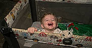 Luxxon is registered to the contest to win money with this photo: blanket, box, carpet, chair, child, clothing, cute, expression, face, furniture, happy, home, indoor, lamp, mesh, person, playpen, smiling, toddler, toy