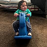 toddler, child, toy, rocking_horse, indoor, carpet, green_sweatshirt, curly_hair, smile, happy, living_room, couch, pillow, striped, pants, footwear, hands, face, person, play