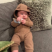 Paulo joined the competition — help win amazing prizes! baby, child, pacifier, hooded_outfit, brown_clothing, couch, pillow, giraffe_pattern, orange_flower, indoor, sitting, striped_socks, curious_expression, plush_furniture, cozy, infant, cute, portrait, home, relaxed