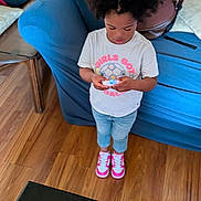 Zuri joined the competition — help win amazing prizes! child, girl, standing, indoor, playing, gadget, white_tshirt, jeans, pink_sneakers, wooden_floor, blue_couch, hair, focused, casual_clothing, young, person, floor, furniture, technology, home
