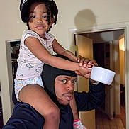 Zuri is registered to the contest to win money with this photo: black_hoodie, cap, casual_clothing, child, cup, door, expression, holding, home, indoor, lighting, man, person, playful, portrait, room, shoulders, socks, tiled_floor, watch