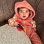 Lilia joined the competition — help win amazing prizes! baby, child, hoodie, pink_clothing, toy, couch, brown_furniture, expression, surprised, indoor, seated, person, infant, face, hand, colorful_toy, plush, cozy, texture, casual