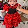 baby, bow, child, cute, flamenco_style, flowers, framed_picture, hand, happy, headband, home, indoor, person, plant, polka_dots, portrait, red_dress, smiling, table, vase