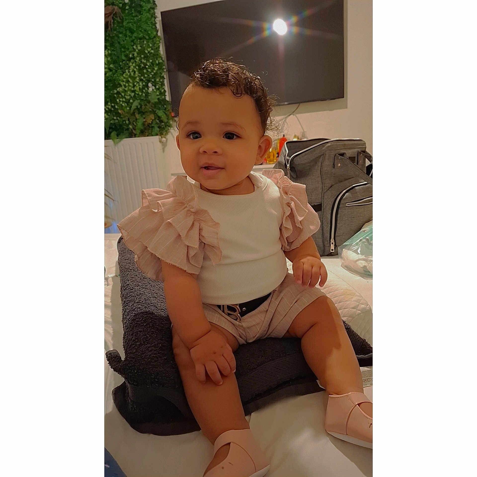 Marie-L'Or participe au concours pour gagner de l'argent avec cette photo : baby, bag, child, comfortable, curly_hair, cute, furniture, home, indoor, infant, person, pink_clothing, plant, portrait, shoes, sitting, smiling, soft_lighting, television, towel