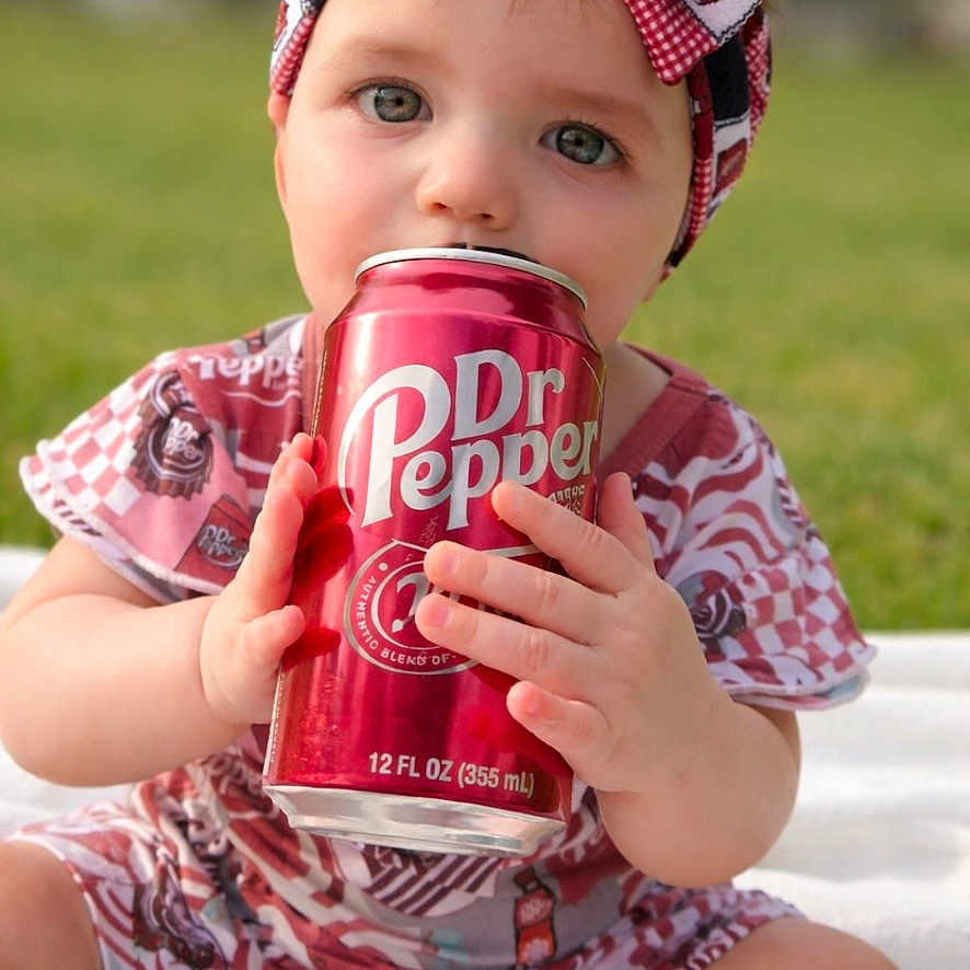Adaline is registered to the contest to win money with this photo: baby, child, headband, bow, drink, can, sitting, outdoor, grass, blanket, cute, portrait, clothing, red, white, person, hands, face, eyes, bottle