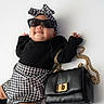 baby, child, sunglasses, black_purse, houndstooth_pattern, headband, fashion, legs, black_clothing, white_background, accessory, cute, smiling, posing, leg_warmers, gold_chain, infant, style, portrait, laying_down